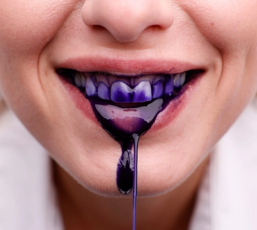 ústa ženy, z ktorých sa tečie fialová zubná pasta