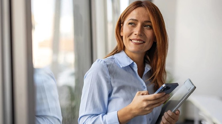 Žena v modrej košeli držiaca smartfón pozerajúca do boku