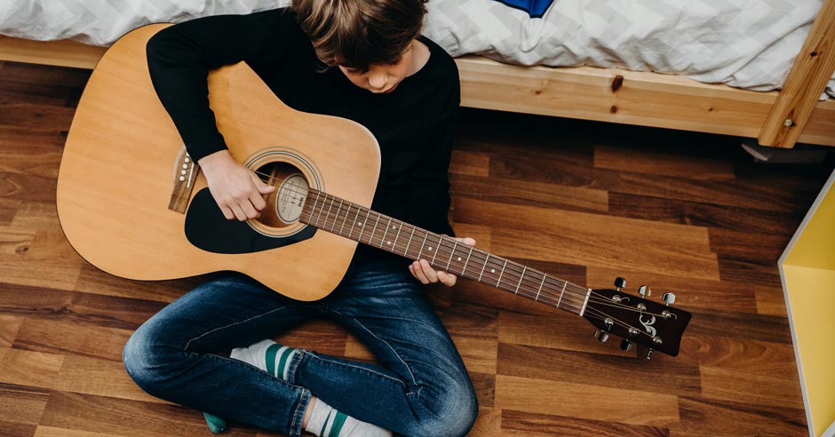 mal&yacute; chlapec sed&iacute; na podlahe v izbe a hr&aacute; na gitare